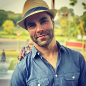 Jason Decker wearing straw fedora hat and wearing a blue button up shirt