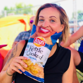 Woman in black shirt holding a chip bag to her face with a smile on it