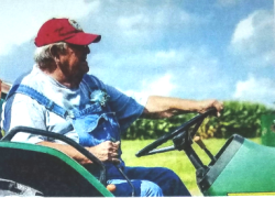 Bill Helms driving a tractor wearing blur overalls and a red hat