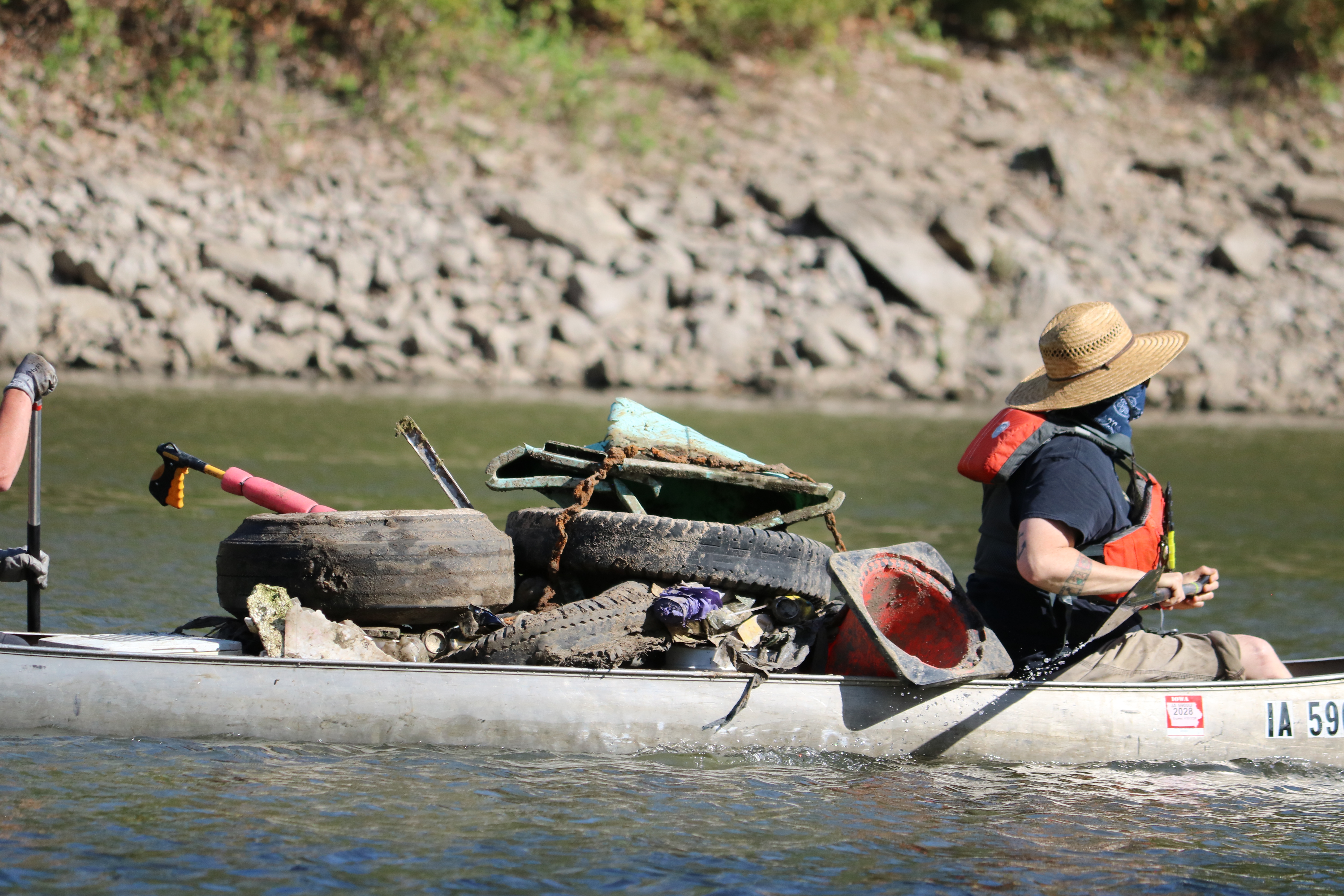Volunteers paddle a canoe that is loaded with tires and other junk removed from the Iowa River.